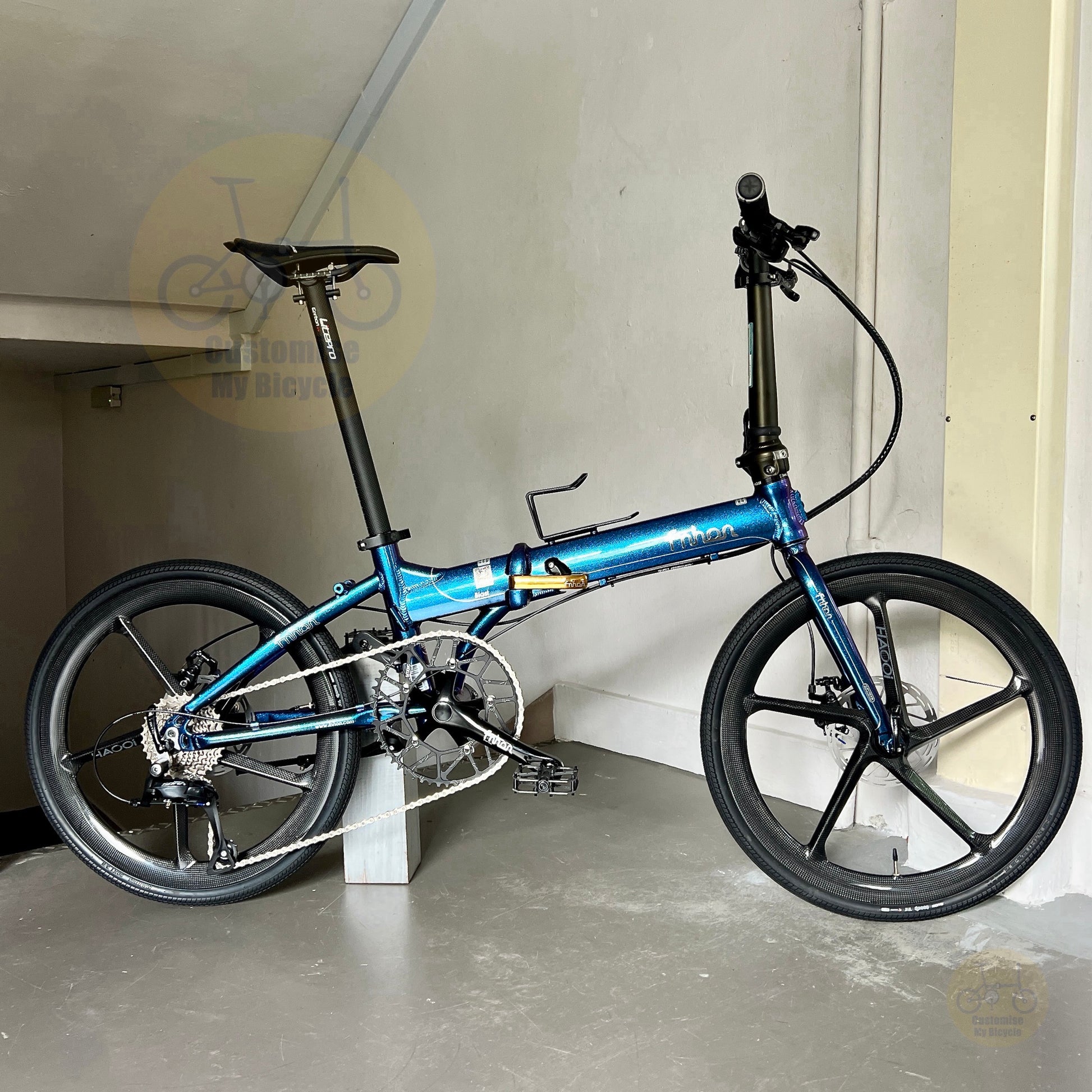 A blue and black folding bicycle with 20-inch wheels, shown in a garage setting with a concrete floor and beige walls.