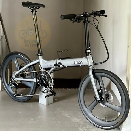 A folding electric bicycle with a silver frame and black components, photographed indoors against a beige wall. The bike has a visible 'fnhan' logo on the main tube and 'Borama' branding on the wheel spokes.
