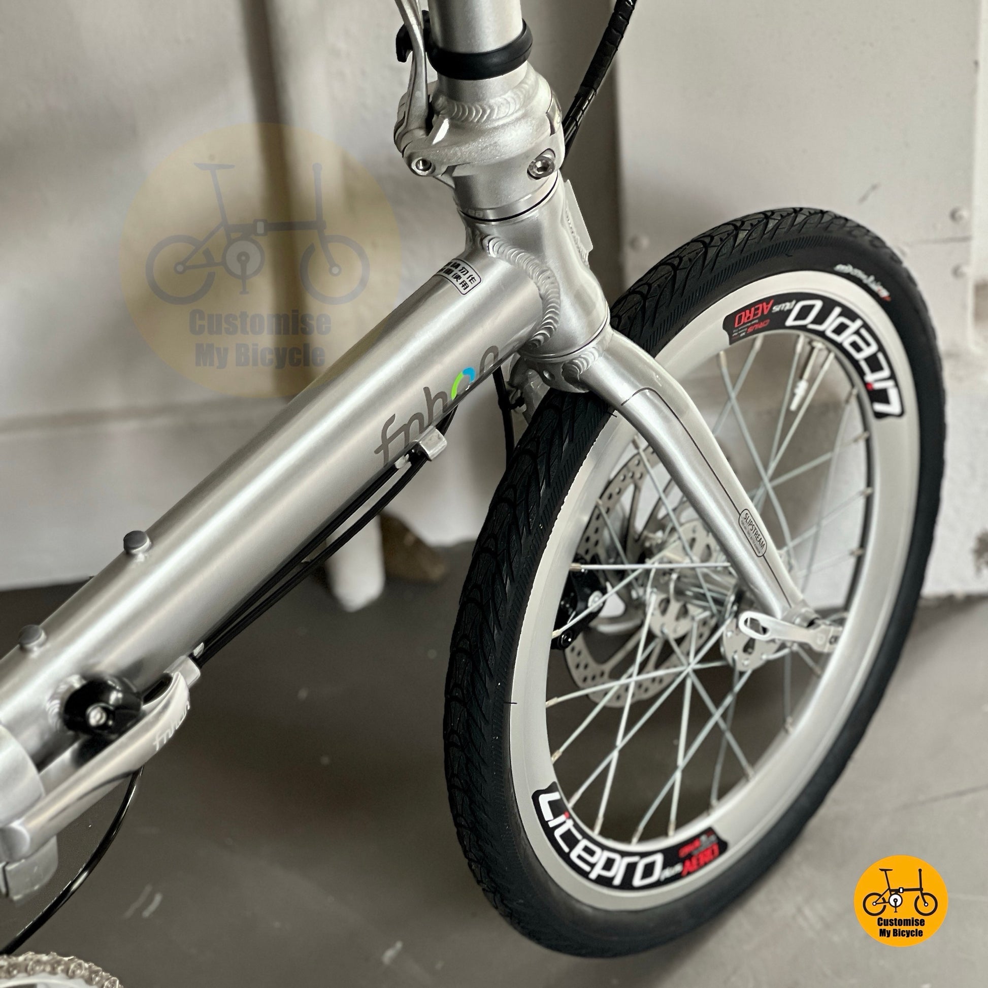 Front wheel and disc brake of Fnhon Zephyr polished silver, featuring Litepro rim and clean spoke design under warm light.
